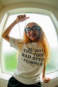 a woman holding up a t - shirt that says don't be the first bad bitch fumble